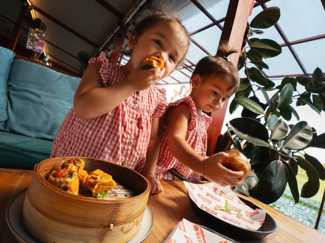 Two children sharing steamed buns at a sunny table