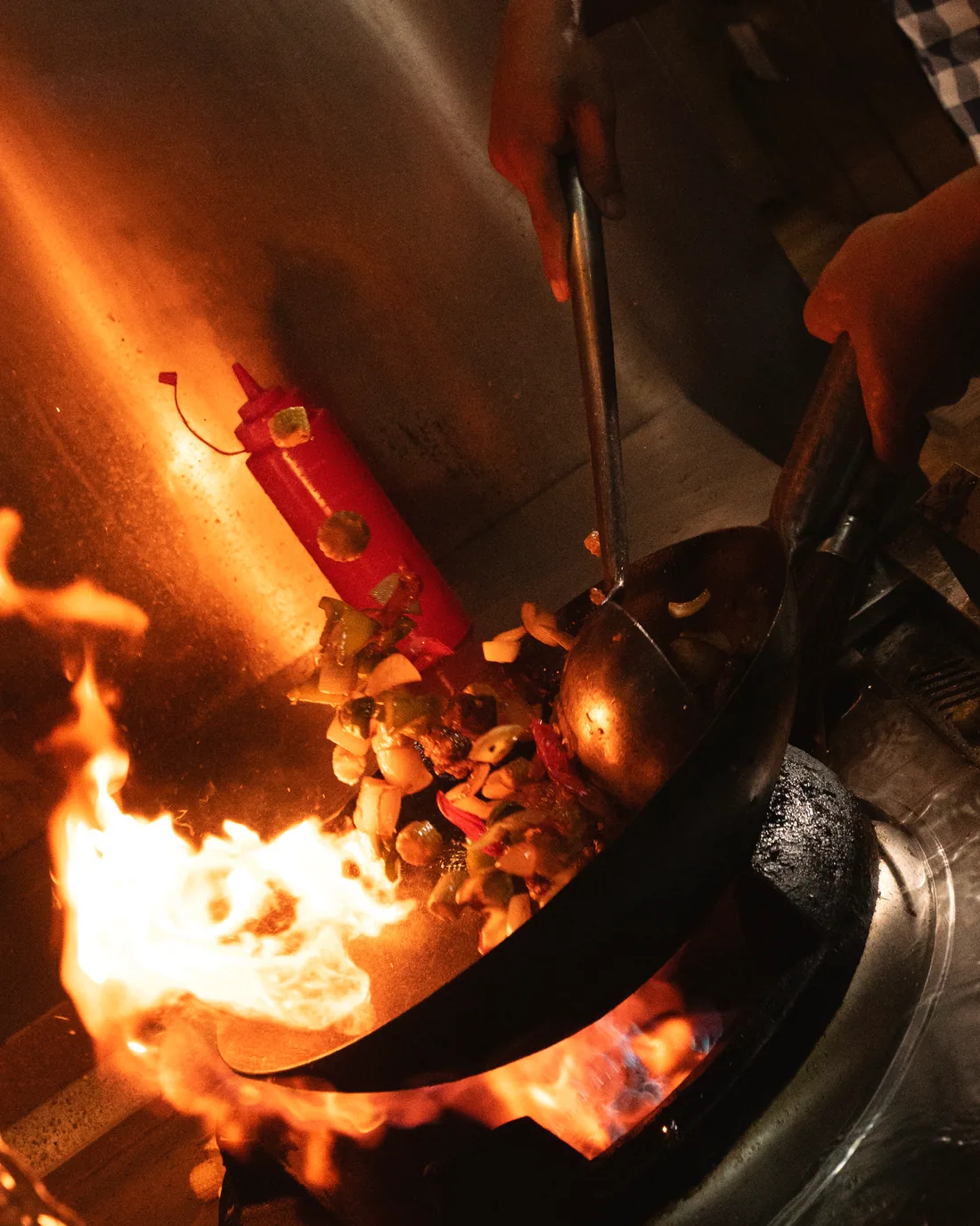 A chef tossing a wok over an open flame