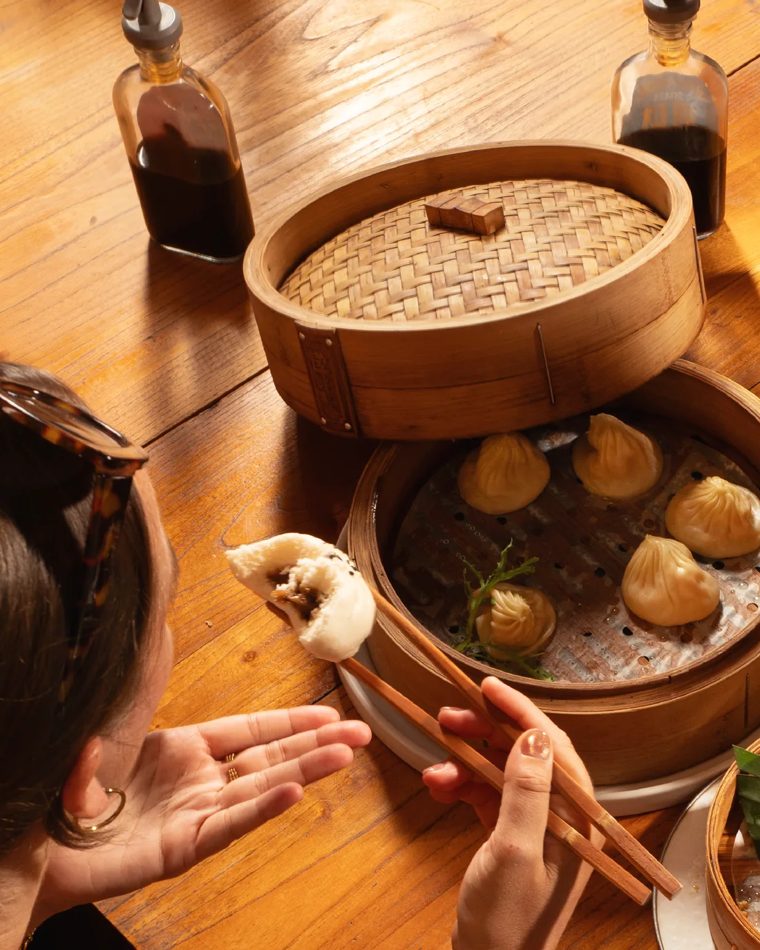 Hand lifting a steamed bun from a bamboo steamer