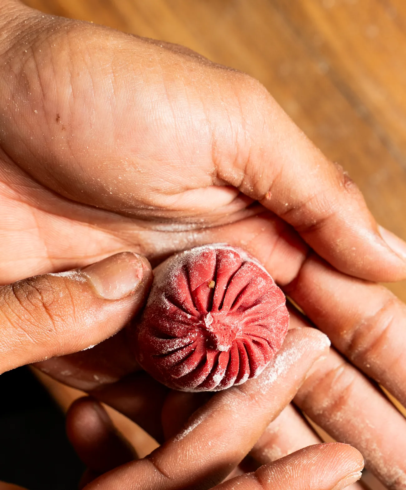 Two hands folding a fresh dumpling by hand, dusted with flour